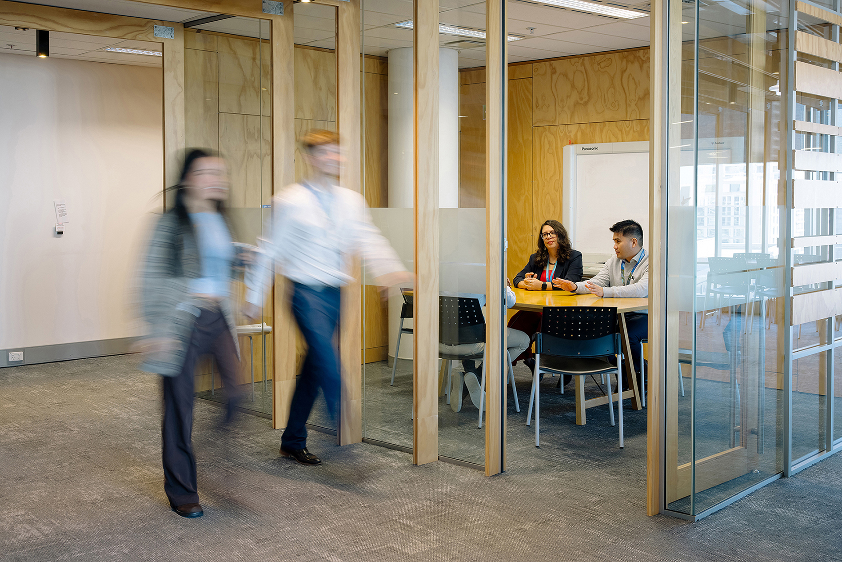 People seated at a meeting room with a couple of people walking by